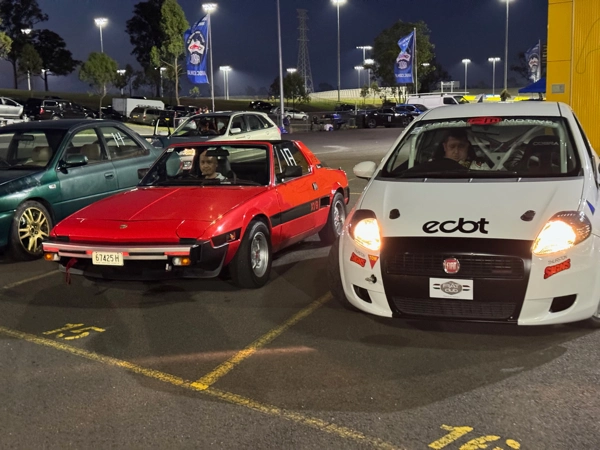 Fiat X1/9 with a Dallara wide-body kit jacked up in the pits for inspection.